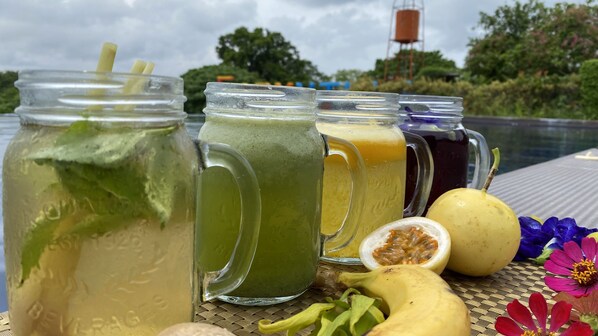 A table with four glass jars containing different beverages, a half-cut fruit, and some flowers.
