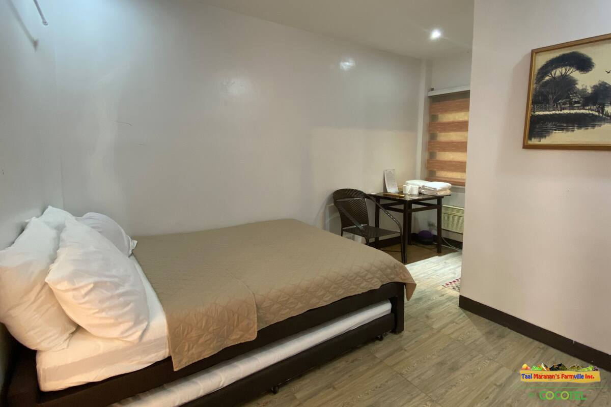 A hotel room with a bed, a chair, a small table with a lamp, and a painting on the wall.