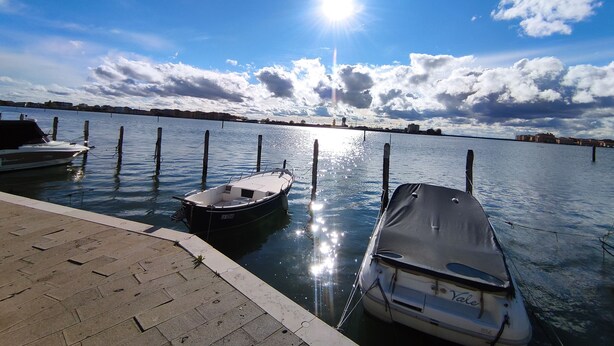 En lysthavn med både i havnen, roligt vand og en klar himmel med skyer.