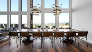 Ein geräumiger Essbereich mit einem langen Tisch und Stühlen, großen Fenstern mit Blick auf die Landschaft und moderner Pendelleuchten.