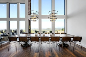 Un comedor amplio con una mesa larga y sillas, ventanas grandes que ofrecen vistas al paisaje, e iluminación colgante moderna.