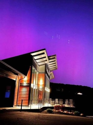 Een modern gebouw met een glazen gevel en een schuin dak, verlicht met warme verlichting.