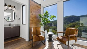 Ein modernes Interieur mit einer schiebbaren Holztür, einem großen Fenster mit Blick ins Grüne und zwei Ledersesseln.