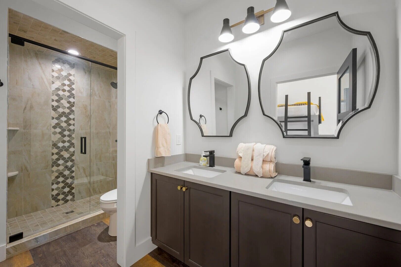 A modern bathroom with two sinks, dark wooden cabinets, and a large mirror with three lights.