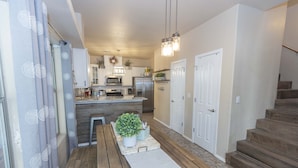 A modern kitchen with white cabinets, a central island, and stainless steel appliances. There is a wooden bench and a small potted plant on the island. - Year Round Heated Pool, Hot Tub, Pet Friendly (Las Cruces)