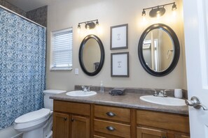 Une salle de bain avec deux lavabos, des toilettes et une douche. Des citations inspirantes encadrées ornent le mur.
