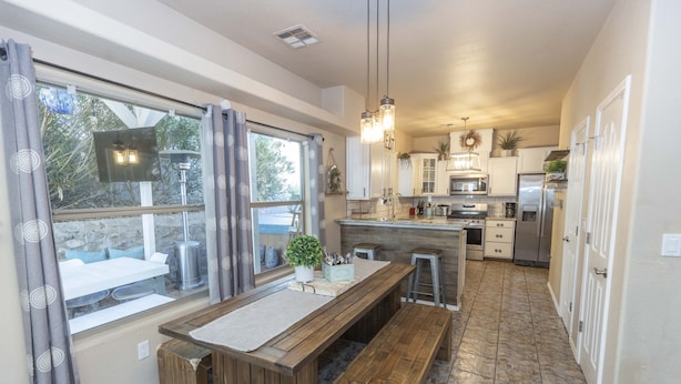 A modern kitchen with a wooden island, bar stools, and a large window with curtains. - Year Round Heated Pool, Hot Tub, Pet Friendly (Las Cruces)