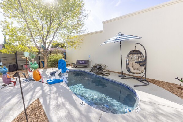 Un jardin avec une piscine, un arbre, une chaise et une cage à oiseaux suspendue.