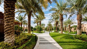 A pathway lined with palm trees and greenery, leading to a building with a stone facade. - Dorat Najd Resort (Diryah)