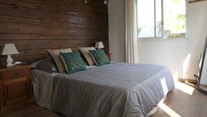 Ein Schlafzimmer mit Holz-Kopfteil, einem Bett mit grauem Bettzeug, zwei Nachttischlampen und einem Fenster mit Vorhängen.
