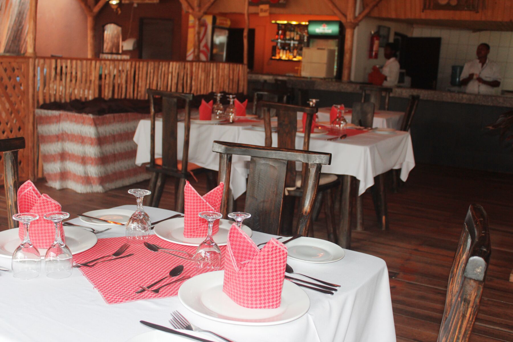 A restaurant with wooden furniture, white tablecloths, and red napkins.