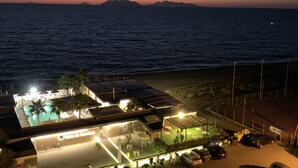 Ein Küstenhotel mit Pool, Sitzgelegenheiten im Freien und Blick auf Meer und Berge im Abendlicht.
