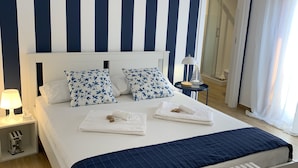 Ein Hotelzimmer mit Bett, weißen Nachttischen, einem Nachttisch, einer Dusche und einer Bank.