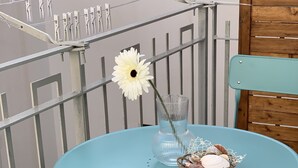 Ein tisch in petrolfarbenem Metall mit einer Glasvase, die eine weiße Blume und ein Korb voll Meeresschnecken enthält.