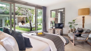 Un dormitorio con una cama grande, televisión, sofá y vistas a una piscina y jardín.