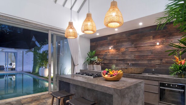 Una cocina moderna con una isla grande, taburetes de bar, protector contra salpicaduras de madera y vista a una piscina.
