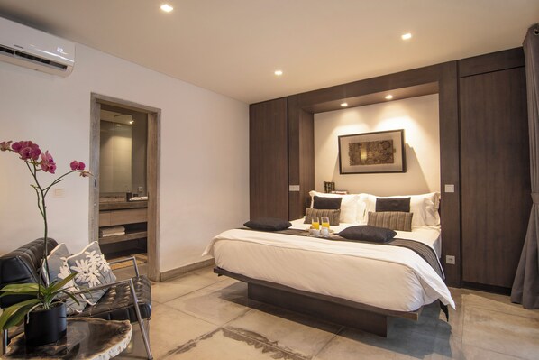 Une chambre à coucher moderne avec un grand lit, des tables de chevet, une plante en pot et un tableau encadré au mur.