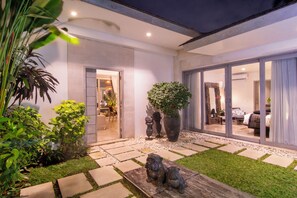 A well-lit outdoor area with a stone pathway leading to a glass door entrance. There are potted plants and a small wooden bench. - Villa Mia by Villa Finder (Canggu)