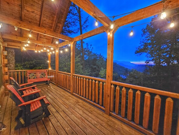 Une terrasse en bois avec une rambarde, des guirlandes lumineuses et deux chaises rouges.