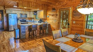 A wooden cabin interior with a kitchen, dining area, and a door with a sign. - New Year Specials - Gorgeous 5 Star Mtn Views - King Beds - Hot tub - Grill (Sevierville)