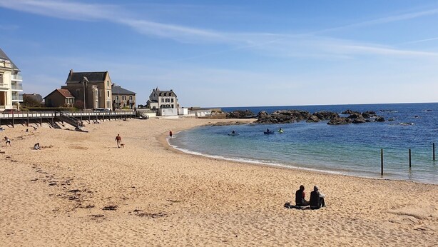 A sandy beach with a pier, rocky shoreline, and buildings in the background. - Wild coastline, exceptional sea view, close to shops and TGV station (Le Croisic)