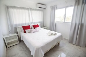 Relax in a serene space with a large bed, nightstand, and window with white curtains.