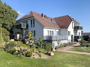 Ein zweistöckiges Haus mit einem geneigten Dach, einem Balkon und einem Garten mit verschiedenen Pflanzen und Blumen.