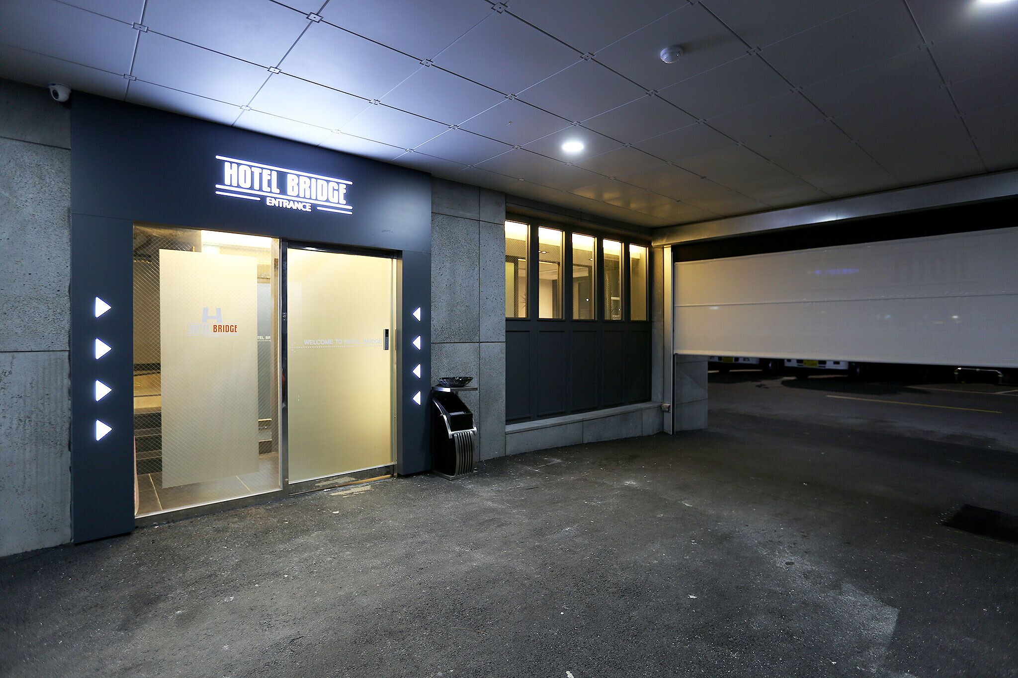A hotel entrance with a sign reading "HOTEL BRIDGE ENTRANCE" and a trash bin outside.