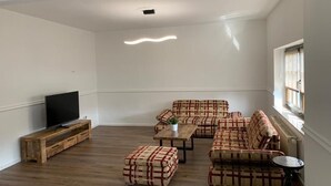 A spacious living room with a wooden floor, a flat-screen TV on a wooden stand, a coffee table, and a sofa set with patterned cushions. - Spreezeit Hotel connect (Senftenberg)