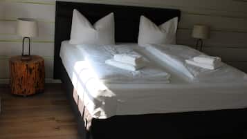 Un lit bien fait, avec du linge de lit blanc et des oreillers, une petite table d’appoint ronde en bois surmontée d’une lampe, et une tête de lit dotée d’un cadre foncé.
