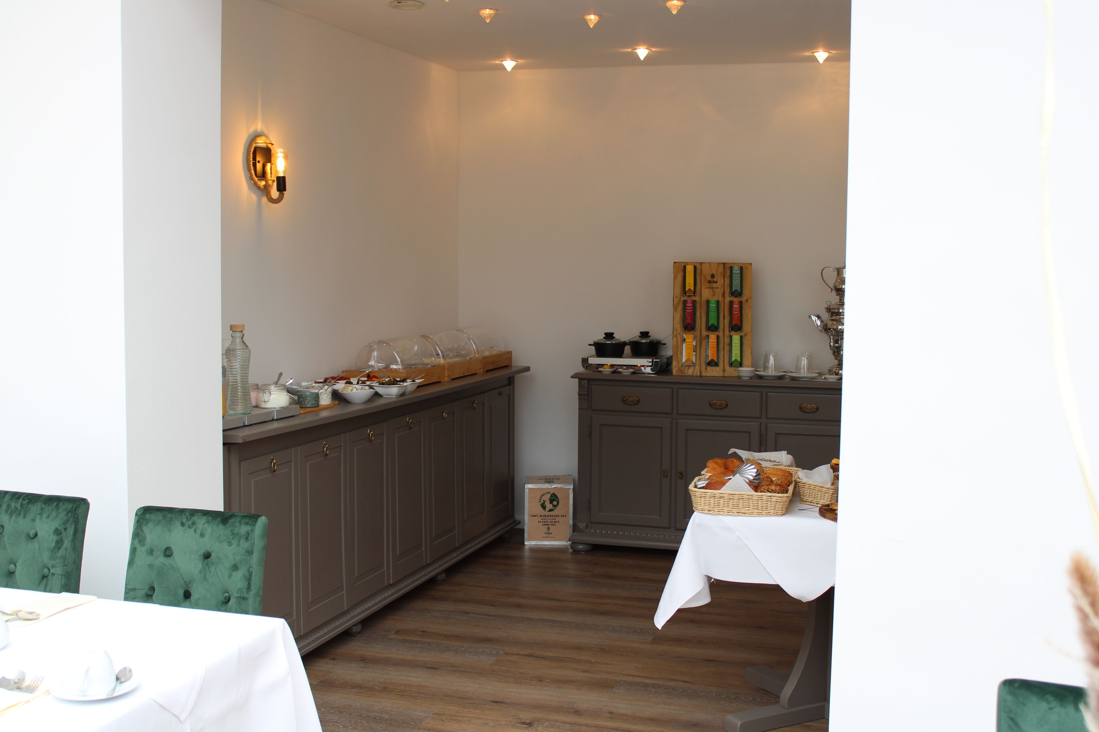 A dining area with a buffet setup, including a table with a white tablecloth and green upholstered chairs.