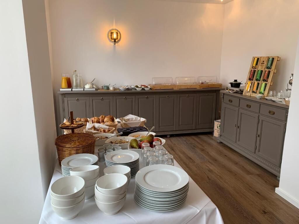 A buffet setup with plates, bowls, and food items on a table, with a kitchen area in the background.