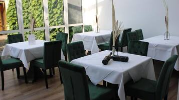 Ein Restaurant mit grün gepolsterten Stühlen und weißen Tischdecken, das in einem großzügigen Essbereich mit großen Fenstern оформлено.