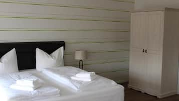 Una cama bien hecha con sábanas y almohadas blancas, una lámpara de noche y un armario blanco en una habitación de hotel.