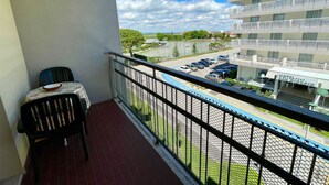 A balcony with a table and chairs, overlooking a parking area and a building with multiple balconies.
