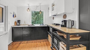 Una cocina moderna con suelo de madera, armarios blancos y encimera negra. Se ve una ventana con vistas a zonas verdes.