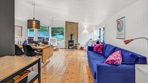 Una sala de estar moderna con piso de madera, un sofá azul, un comedor con mesa de madera y una chimenea de ladrillo.