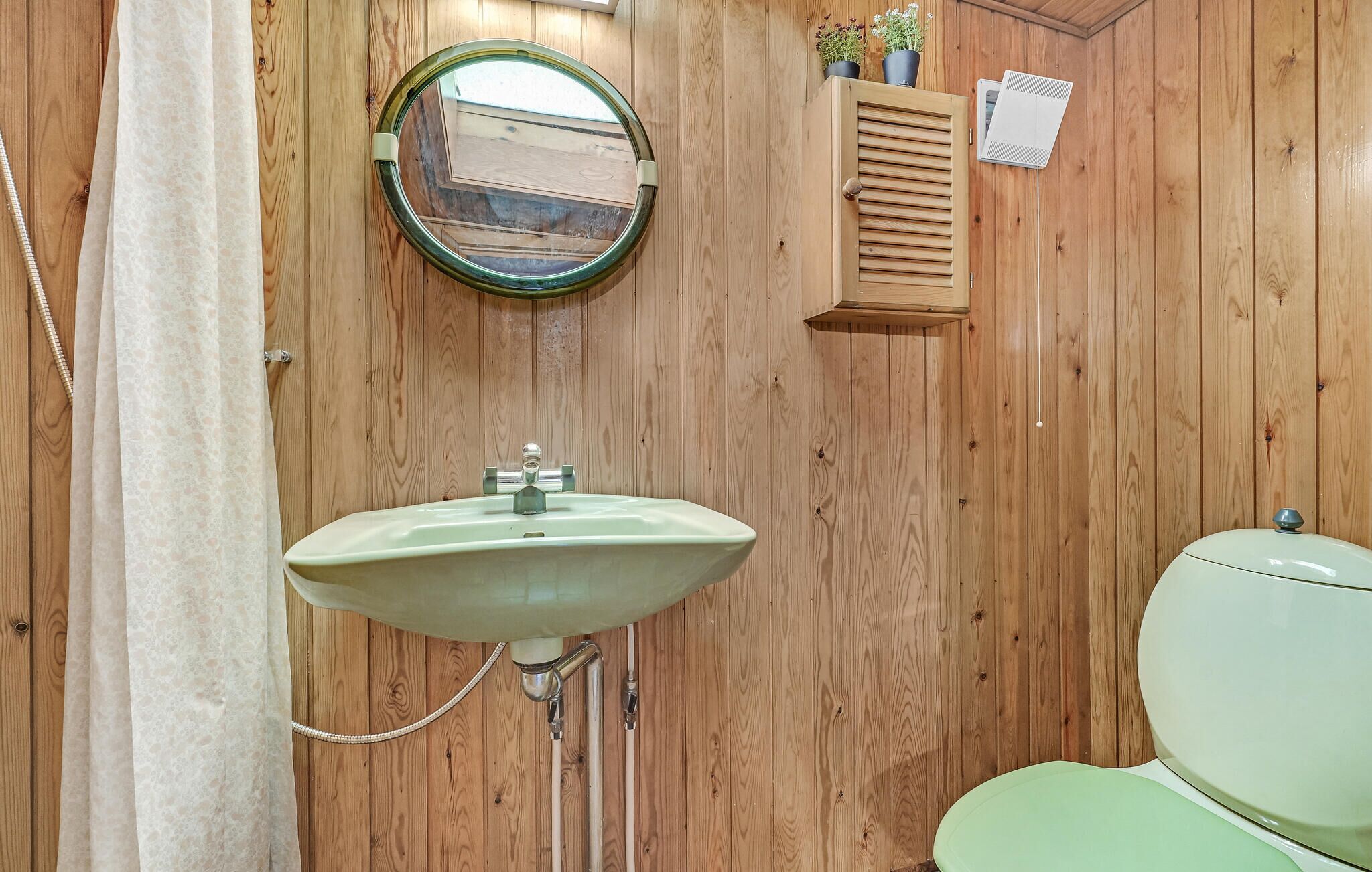 A bathroom with a wooden wall, a round mirror, a sink, and a toilet.