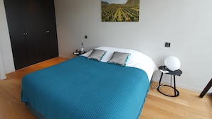 A bedroom with a large bed, a nightstand, a wall-mounted picture, and a wardrobe. - Le Pavillon - The Lion (Néac)
