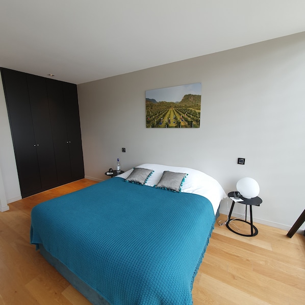 A bedroom with a large bed, a nightstand, a wall-mounted picture, and a wardrobe. - Le Pavillon - The Lion (Néac)