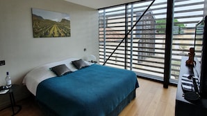 A bedroom with a bed, a painting, a water bottle, and a view through large windows. - Le Pavillon - The Lion (Néac)