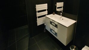 A modern bathroom with a white sink, dark tiles, and a large mirror with lights. - Le Pavillon - The Lion (Néac)
