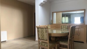 Zona de menjador amb una taula rodona de vidre, quatre cadires, un armari de fusta i un gran mirall a la paret.