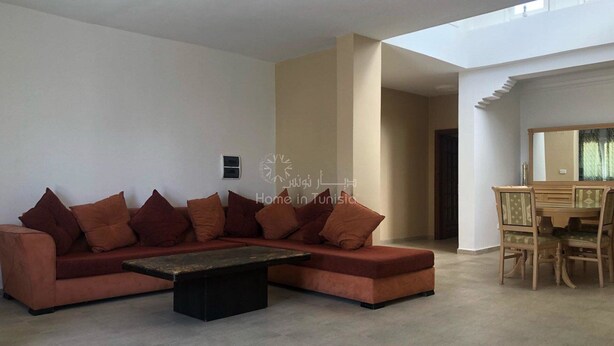 Un saló modern amb un sofà modular, una taula de centre i una zona de menjador amb una taula i cadires de fusta.