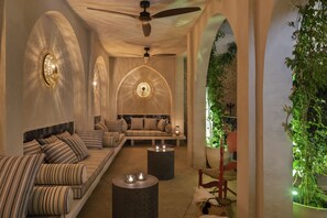 A cozy lounge area with a sofa set, two round tables with candles, a ceiling fan, and a wall-mounted light fixture. - Pájaro Rebelde (Seville)