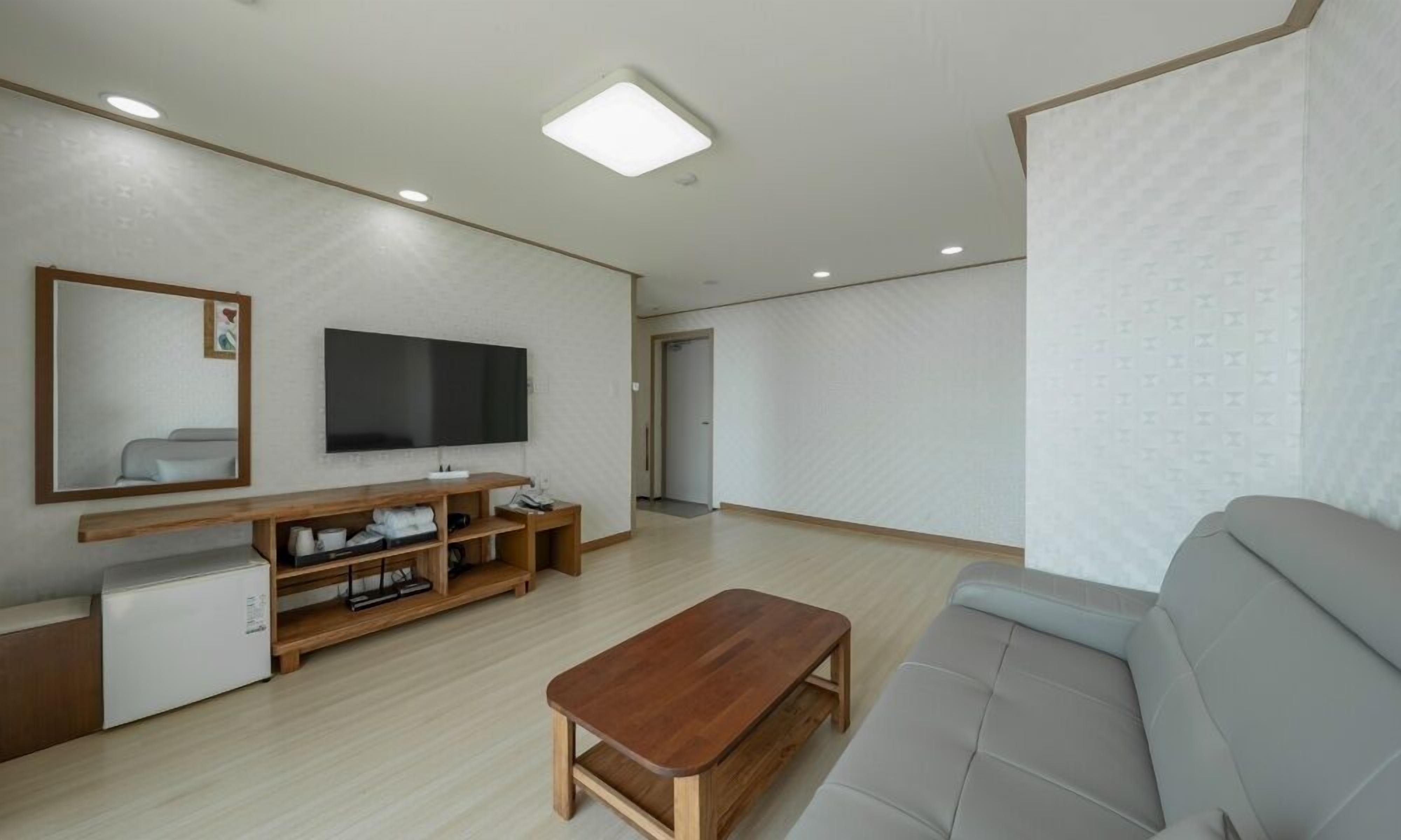 A modern living room with a flat-screen TV, wooden entertainment unit, and a grey sofa.