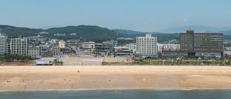 A coastal cityscape with a beach, buildings, and mountains in the background.