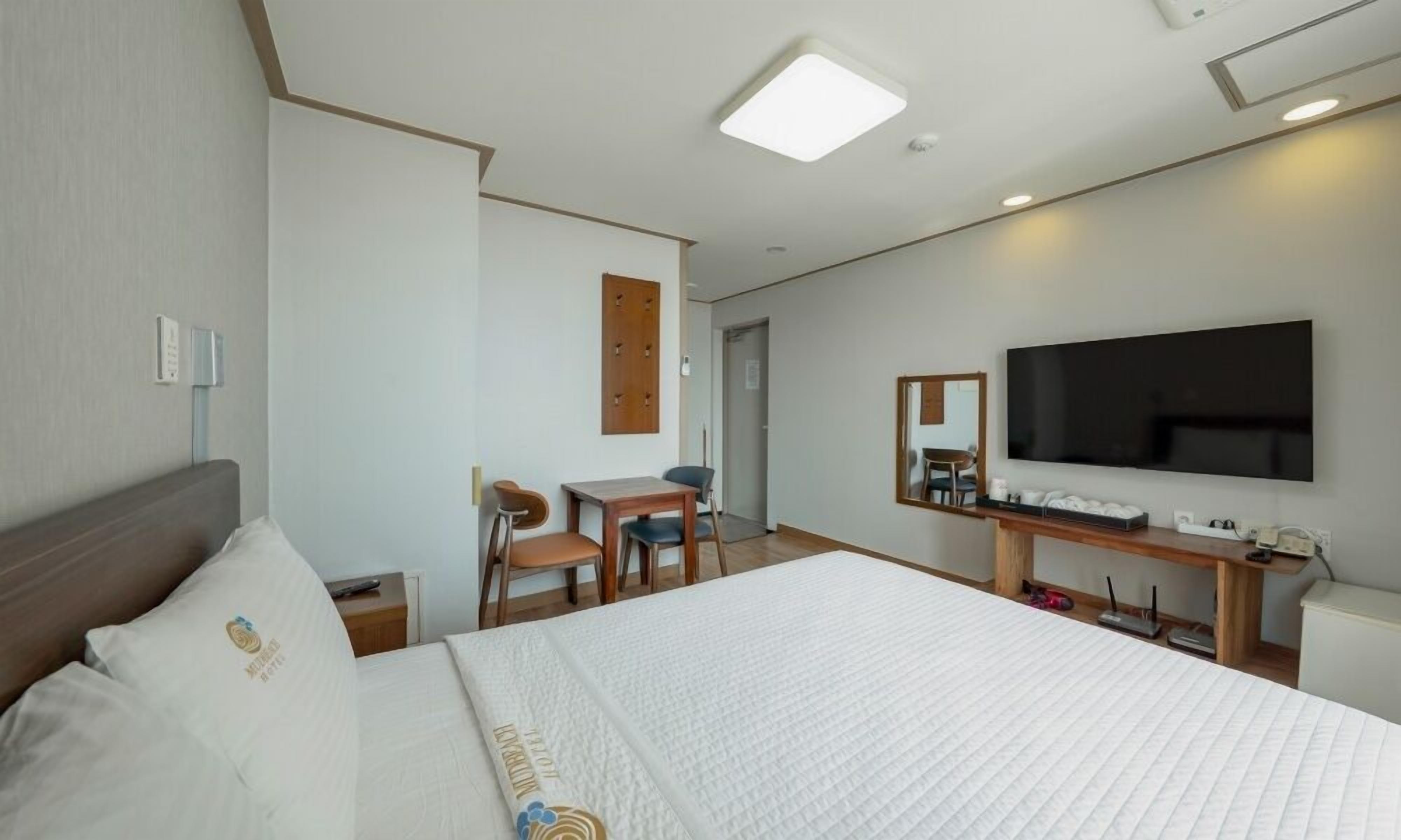 Una habitación de hotel con una cama grande, un escritorio, una silla, un televisor y un espejo.