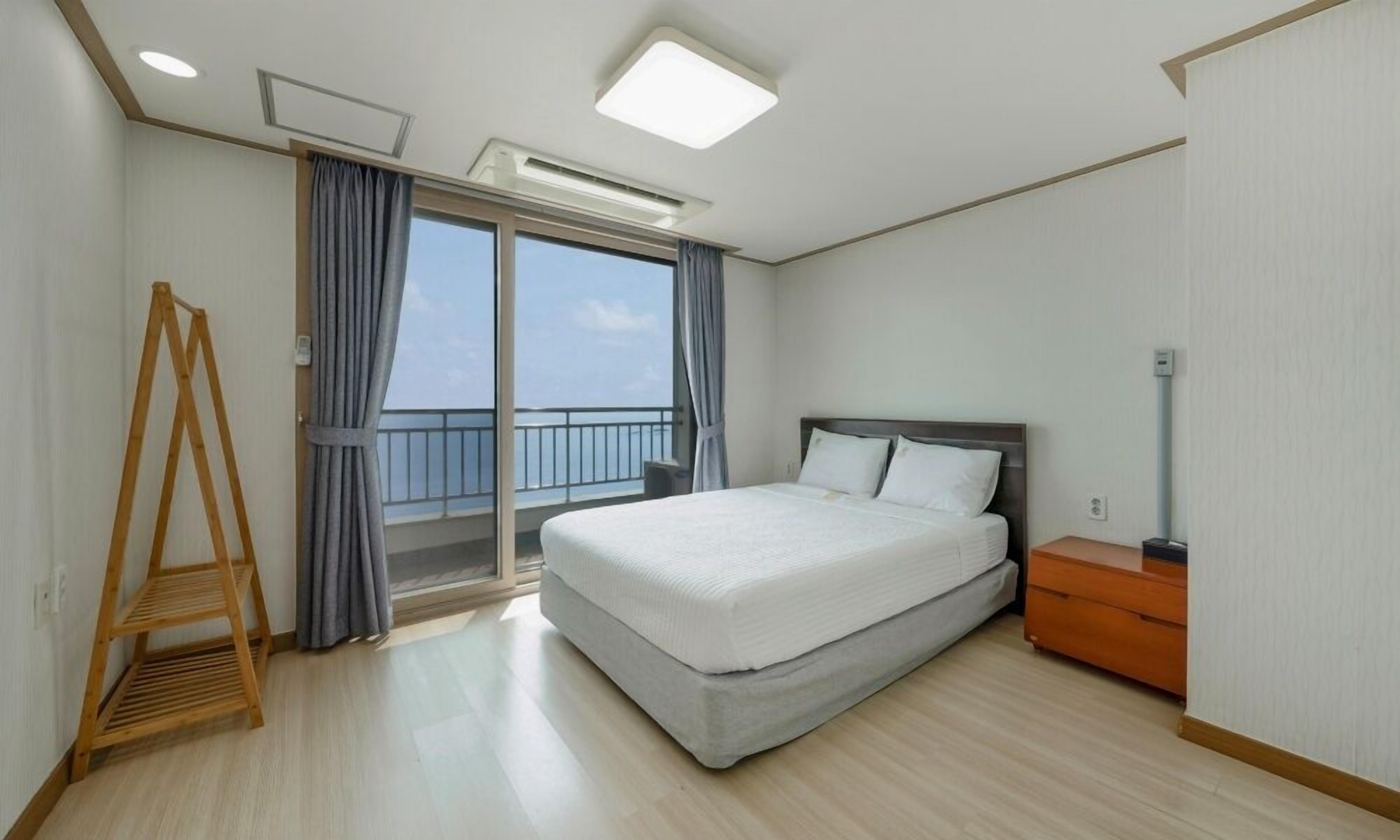 Une chambre d’hôtel avec un lit, une échelle en bois, une table de chevet et une vue sur la mer par une grande fenêtre.