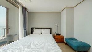 A hotel room with a bed, a nightstand, a blue chair, and a window with curtains. - Daecheon Mud Beach Hotel (Boryeong)